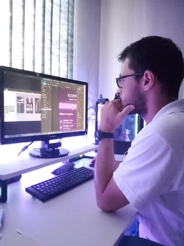 Homem 30 anos sentado com mão no queixo olhando para tela do computador editando um arquivo no Figma